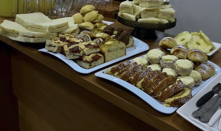 La mesa del desayuno: sándwiches de miga, budines, masitas con dulce, medialunas, piña cortada y jarras de jugo