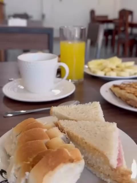 Una mesa servida: café, jugo de naranja, frutas cortadas, tostados, manteca y mermelada