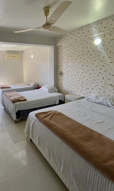 Suite familiar: una cama queen en primer plano y dos camas más hacia el ventanal, con ventilador de techo