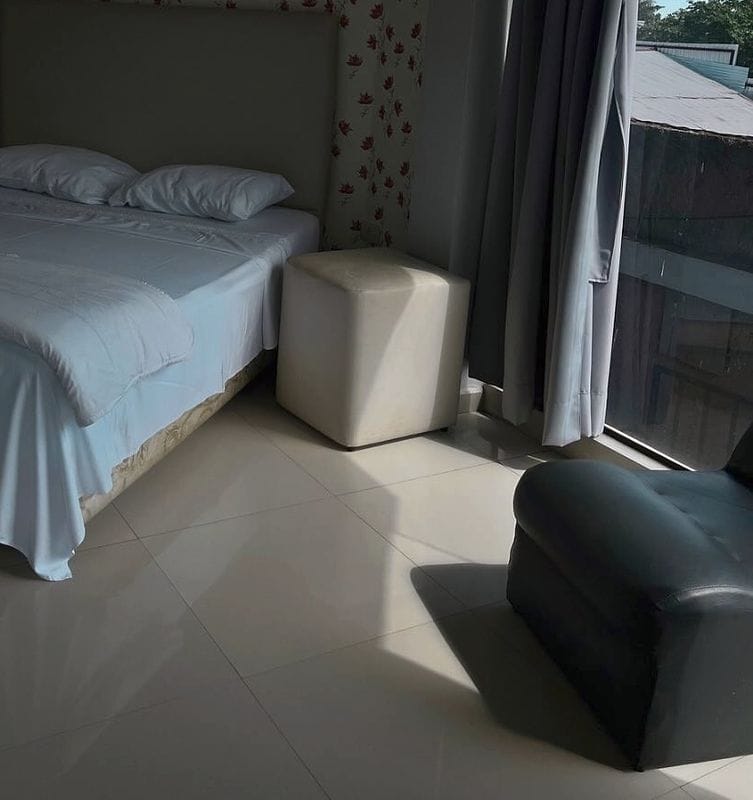 Suite matrimonial: la cama tendida, un puf, la cortina gris y un sillón junto al ventanal