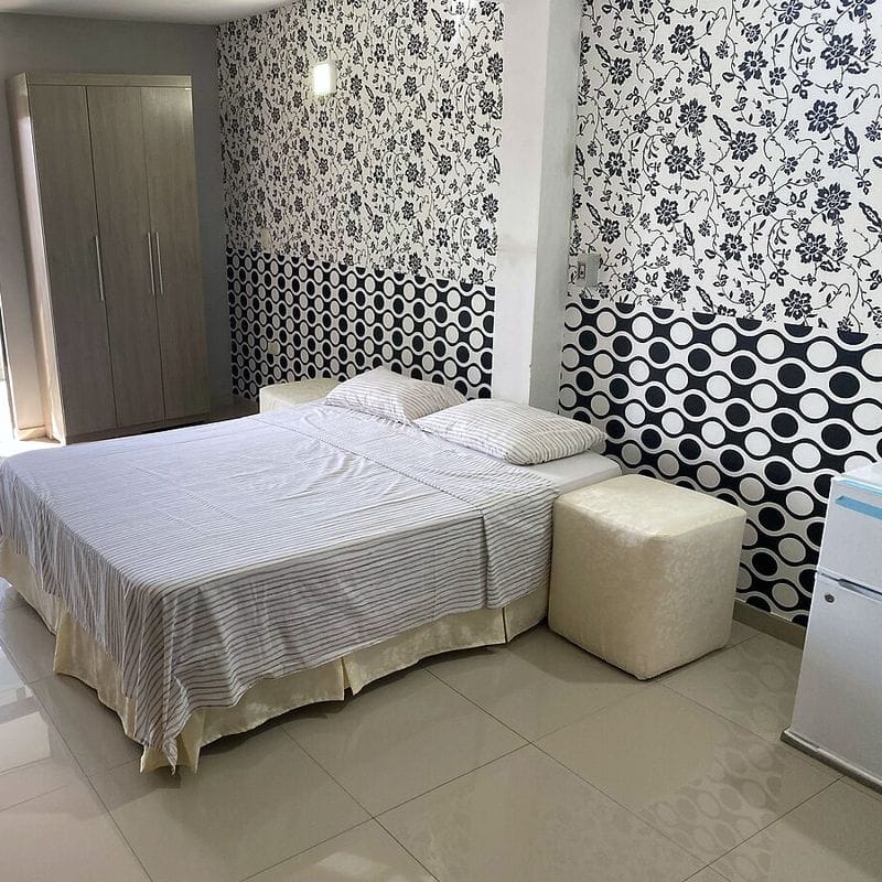 Suite con cama queen: papel tapiz floral en blanco y negro, ropero, un puf y el frigobar