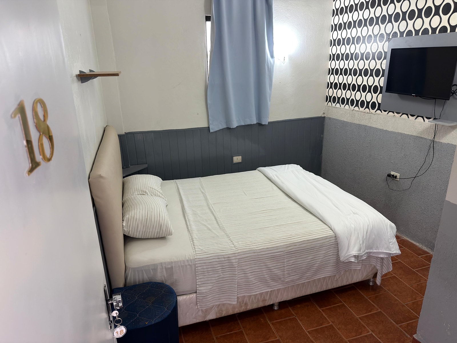 La habitación estándar: una cama matrimonial con almohadones, el televisor en la pared y la puerta número 18