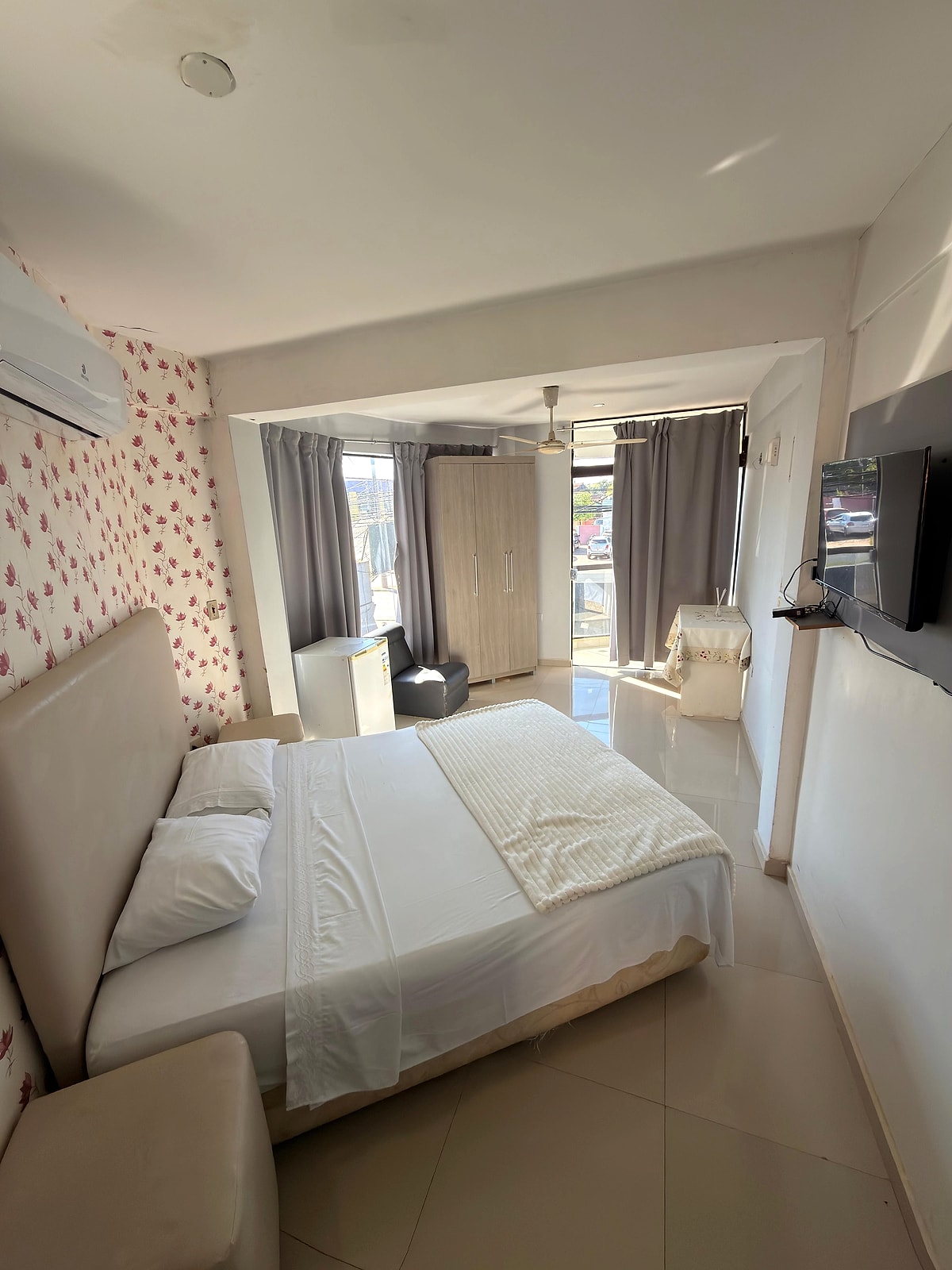 La suite: cama tendida en blanco, el ventanal con cortinas, el aire acondicionado y el televisor