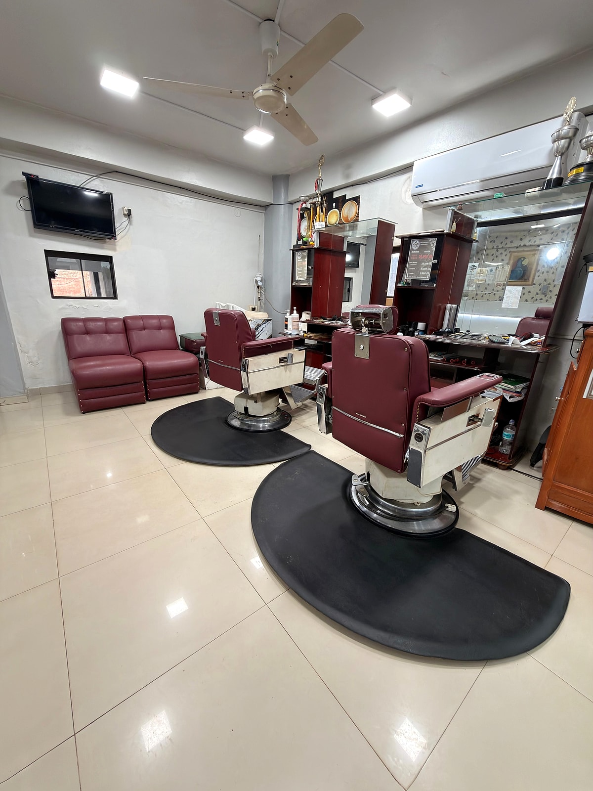La peluquería del hotel: dos sillones de barbero bordó sobre alfombras negras, los espejos y el televisor
