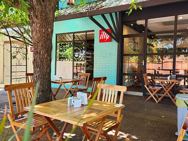 Abril Café: La terraza de la cafetería, con mesas de madera bajo los árboles